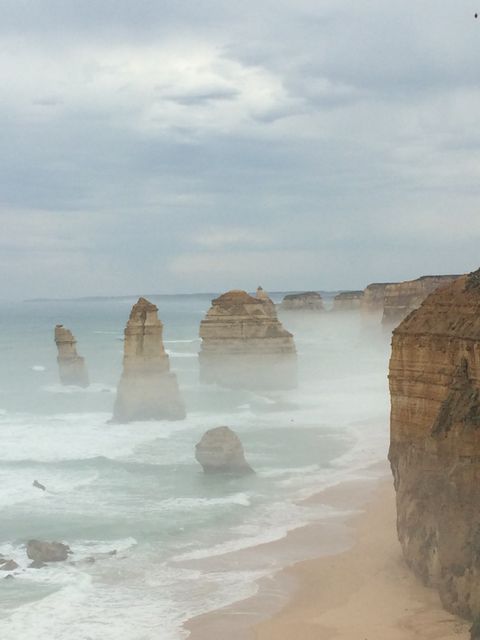 Misty Twelve Apostles sea stacks at dusk on Australia's coast. Features ocean waves crashing against the famous limestone rock formations. The calming mist and rugged cliffs create a serene and picturesque atmosphere. Ideal for travel content, natural landmarks showcases, and coastal scenery themes.