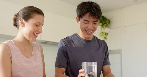 Smiling diverse couple preparing healthy green smoothie in bright modern kitchen