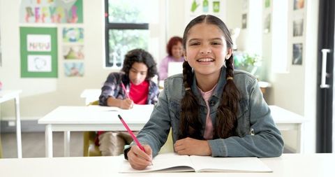 Happy Schoolgirl Writing Enthusiastically in Bright Classroom