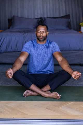 African american man practicing mindful meditation on yoga mat in modern minimalist bedroom