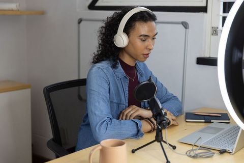 Non-binary podcaster recording with headphones and condenser mic in minimalist studio