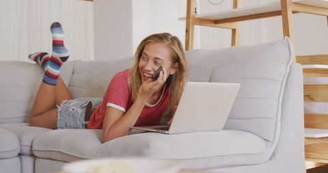Smiling woman relaxing on sofa with laptop and phone on weekend