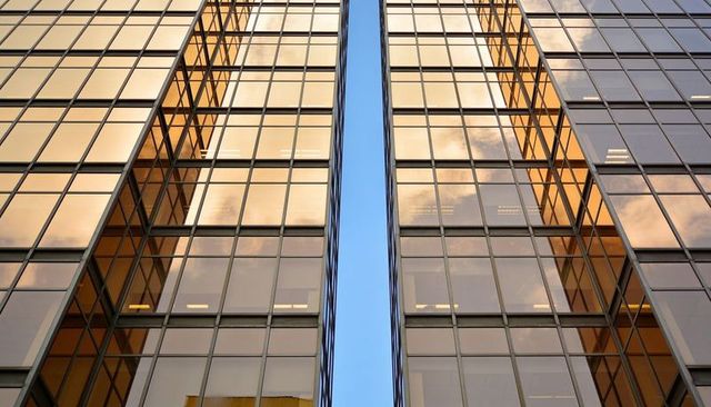 Paired golden glass facades rising with narrow sky gap reflecting urban sunset glow