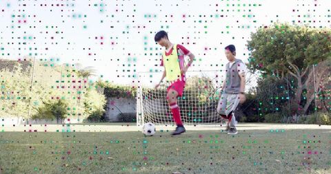 Teenage boys dribbling soccer ball on backyard lawn with goal practicing casual training