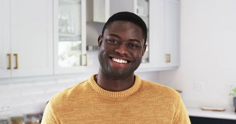 Man smiling in modern kitchen wearing casual mustard sweater