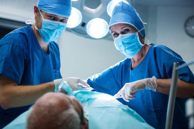 Healthcare professionals working together in a sterile operating room while performing a surgical procedure on a patient. Ideal for use in medical articles, healthcare marketing material, educational content for medical students, or related to surgical advances and hospital care.