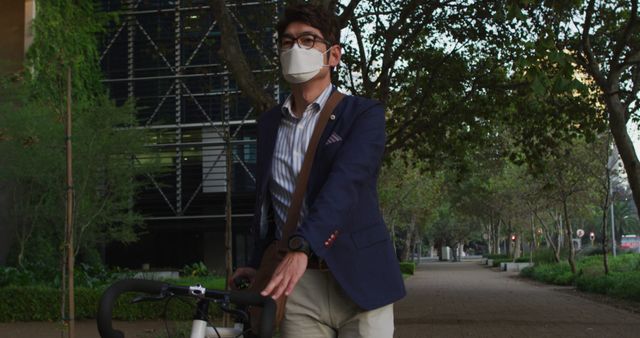 Young businessman commuting to work by bicycle while wearing a face mask, promoting sustainable and healthy transportation. Surrounded by lush trees and urban environments, demonstrating commitment to health safety and eco-friendly commuting amidst Covid-19. Ideal for campaigns related to urban transportation, sustainability, health, and workplace safety.
