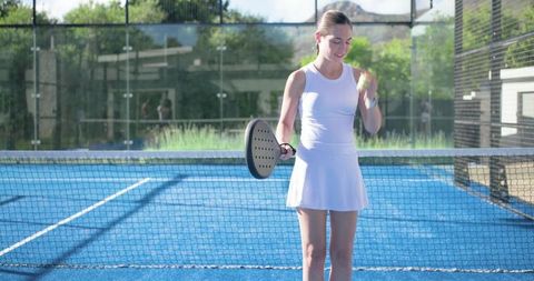 Female athlete practicing padel on sunlit blue court holding racket and ball