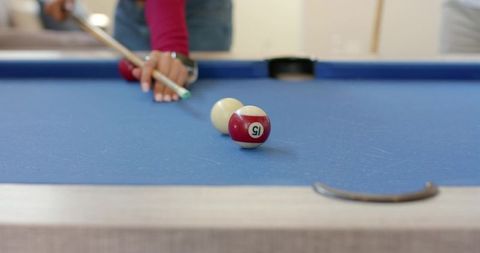 Female leaning over blue felt pool table aiming cue at 15 ball close-up