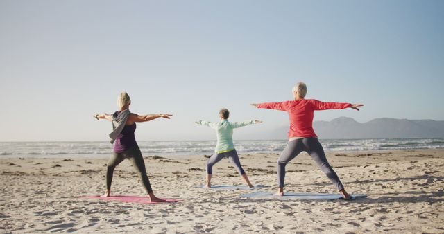Diverse group of senior women doing yoga and stretching at beach. Retirement, friendship, healthy and active lifestyle.