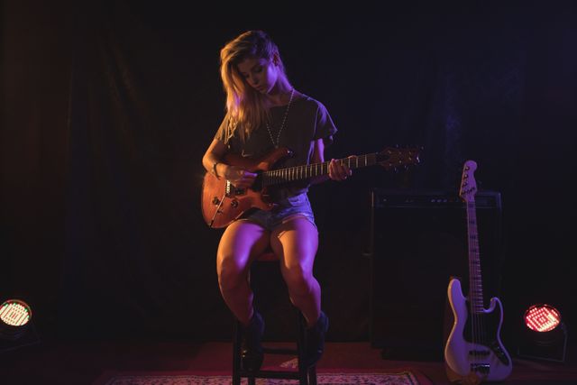 Female musician playing electric guitar on stage in a dimly lit nightclub. Ideal for use in articles about live music, concert promotions, music events, and nightlife entertainment.