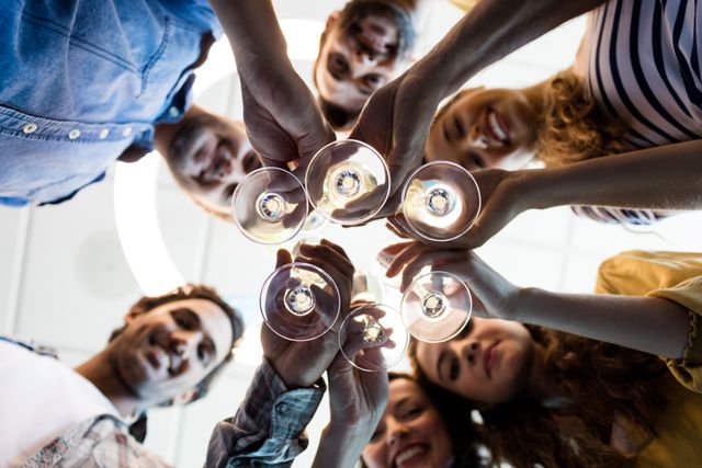 This image shows a diverse group of colleagues toasting with champagne glasses in an office setting, celebrating a special occasion such as a birthday or corporate success. Ideal for use in articles or advertisements about teamwork, corporate culture, office parties, and employee engagement.