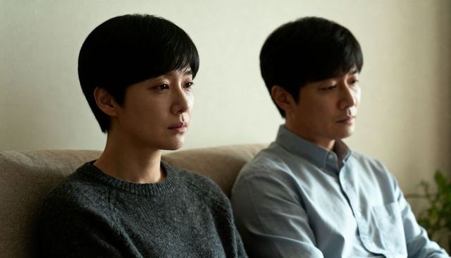 Contemplative asian couple sitting apart on sofa in muted living room minimal interior