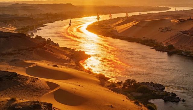 Golden sunset over desert river with feluccas sailing along dunes and reflective waterway