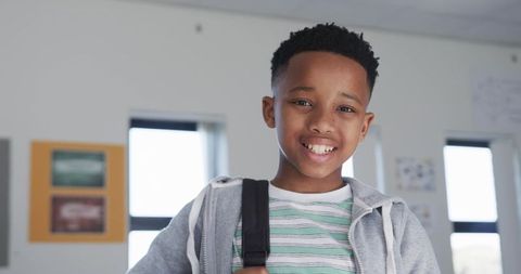 Smiling student holding backpack strap in bright classroom portrait showing confident youth