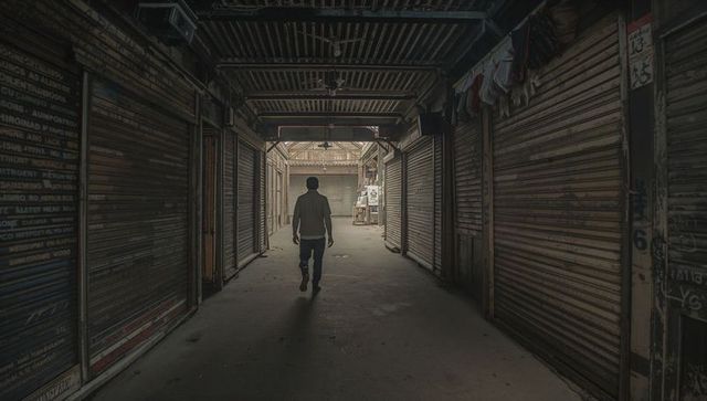 Solitary man walking through dim closed market arcade with metal shutters and graffiti