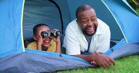 African american father son backyard camping in blue tent laughing with binoculars