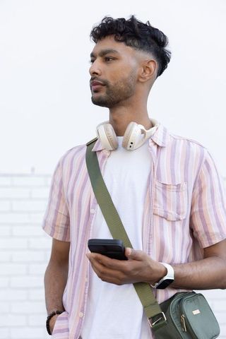 Indian young man wearing headphones and striped shirt checking smartphone in city