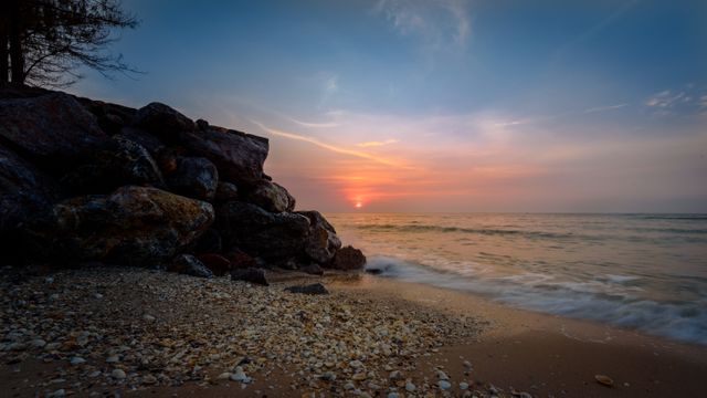 Peaceful sunset on a rocky beach with gentle waves lapping the shore, creating a serene and beautiful scene perfect for backgrounds, travel brochures, nature-themed content, meditation apps, or desktop wallpapers.