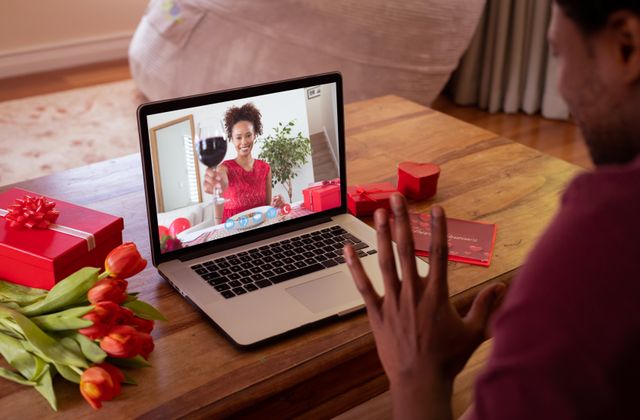 Happy biracial young woman showing red wine to boyfriend during online dating. unaltered, online dating, video call and distant valentine day celebration.