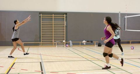 Diverse female volleyball players practicing indoor drill on hardwood court, teamwork motion