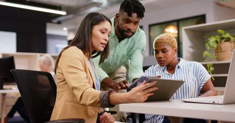 Diverse team collaborating using tablet and laptop in modern office