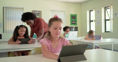 Elementary students using tablets in classroom with teacher assisting digital learning