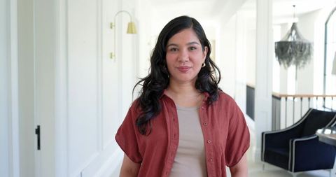 Confident woman standing in minimalist hallway wearing rust overshirt and neutral top