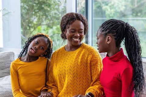 African american mother smiling with daughters on cozy living room sofa in mustard sweater