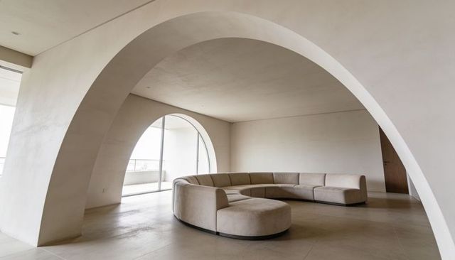 Curved modular sofa nesting under smooth arches in minimalist beige open-plan apartment