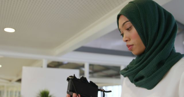 Young Muslim woman examines virtual reality headset in office. She's exploring the potential of VR technology for business applications.