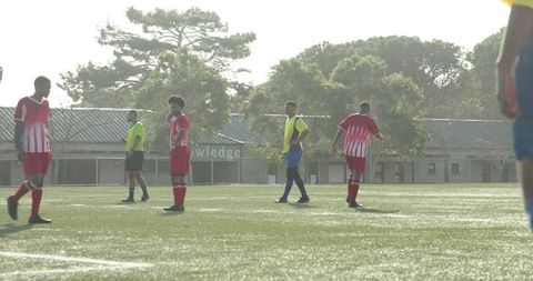 Soccer Players Competing on Sunny Field with Trees in Background