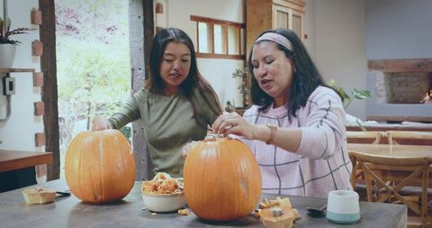 Mother and Daughter Carving Pumpkins Together in Cozy Rustic Kitchen Preparing Halloween
