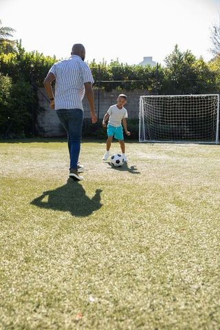Father and son playing soccer by backyard goal