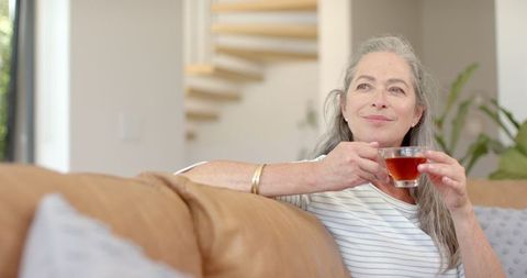 Relaxed mature woman enjoying tea on comfortable couch