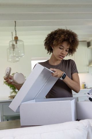 African american woman opening boxes unboxing smart home device on modern kitchen counter