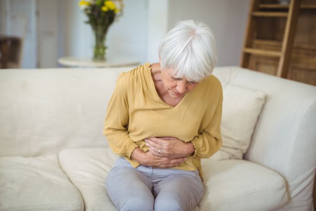 Senior woman suffering from stomach pain in living room at home