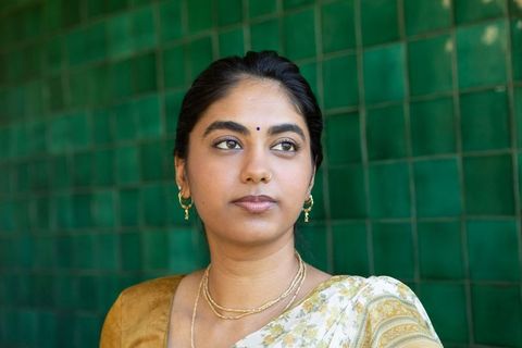Indian woman in sari with gold jewelry against green wall