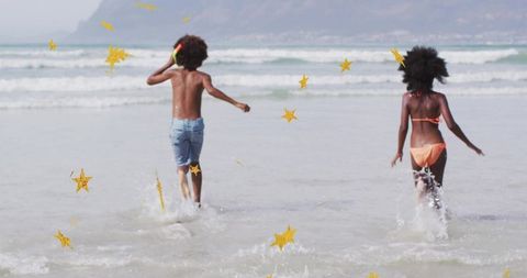 Two kids running and splashing in shallow surf with whimsical gold stars
