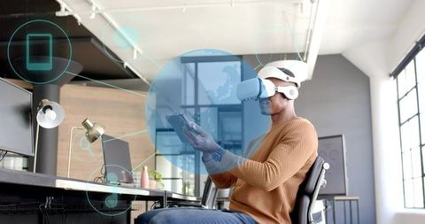 Man wearing VR headset using tablet with holographic interface in bright office