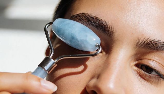 Close-up woman rolling blue jade face roller under eye for de-puffing and skincare ritual