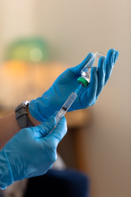 Cropped hands of caucasian doctor wearing gloves holding vial and syringe against white wall at home. Copy space, injecting, medicine, unaltered, healthcare and medical occupation concept.