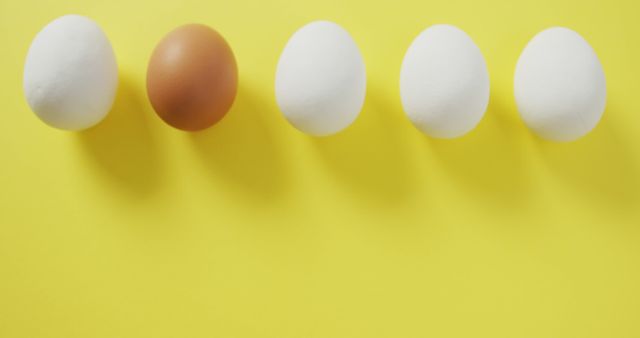 Image of row of one brown and four white eggs on yellow background. fusion food, baking, eggs and easter concept.