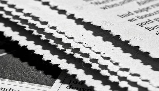Stacked scalloped paper edges revealing fibrous texture dramatic monochrome shadows