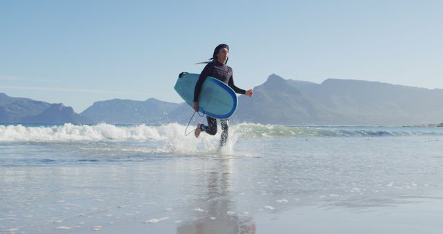 Image of caucasian man with dreadlocks in wetsuit carrying surfboard running from sea to sunny beach. Freedom, sport, hobbies and healthy active lifestyle concept digitally generated image.