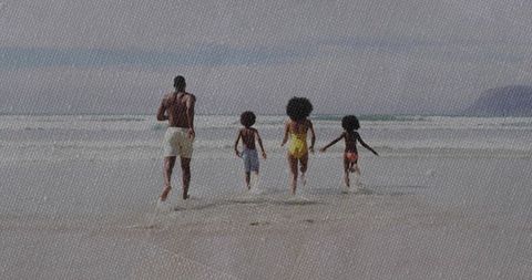 Family running along shoreline into gentle ocean waves on sandy beach