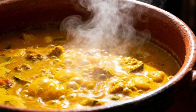 Simmering earthenware curry pot bubbling yellow coconut broth with whole eggs and spice