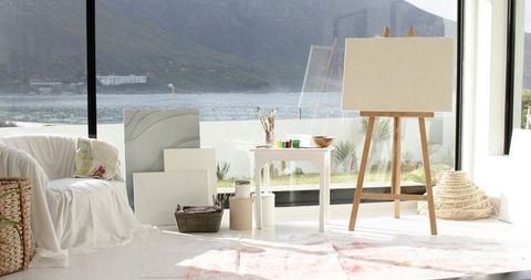 Sunlit artist studio with easel and blank canvas overlooking waterfront and mountains