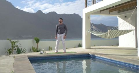 Indian man standing on yoga mat beside pool on luxury coastal villa terrace