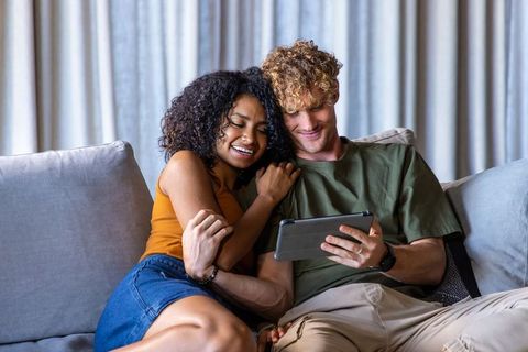 Young couple cuddling on sofa watching tablet, sharing cozy romantic moment at home